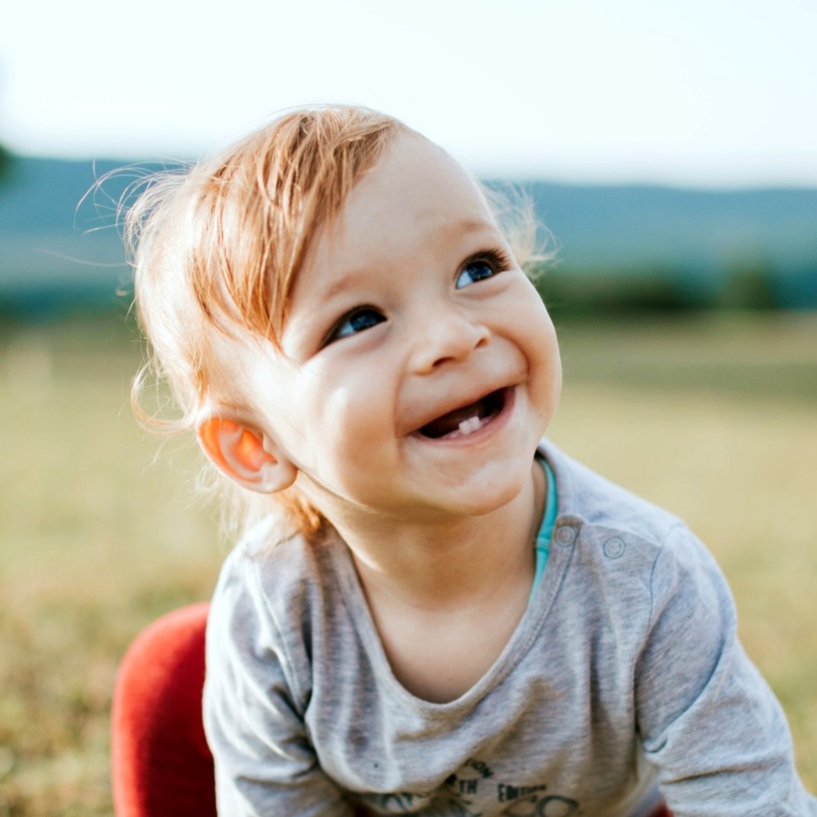 A child looking up with only two bottom teeth showing through their smile